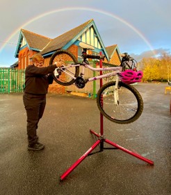 Woman fixing a bike on a stand with a rainbow behind her