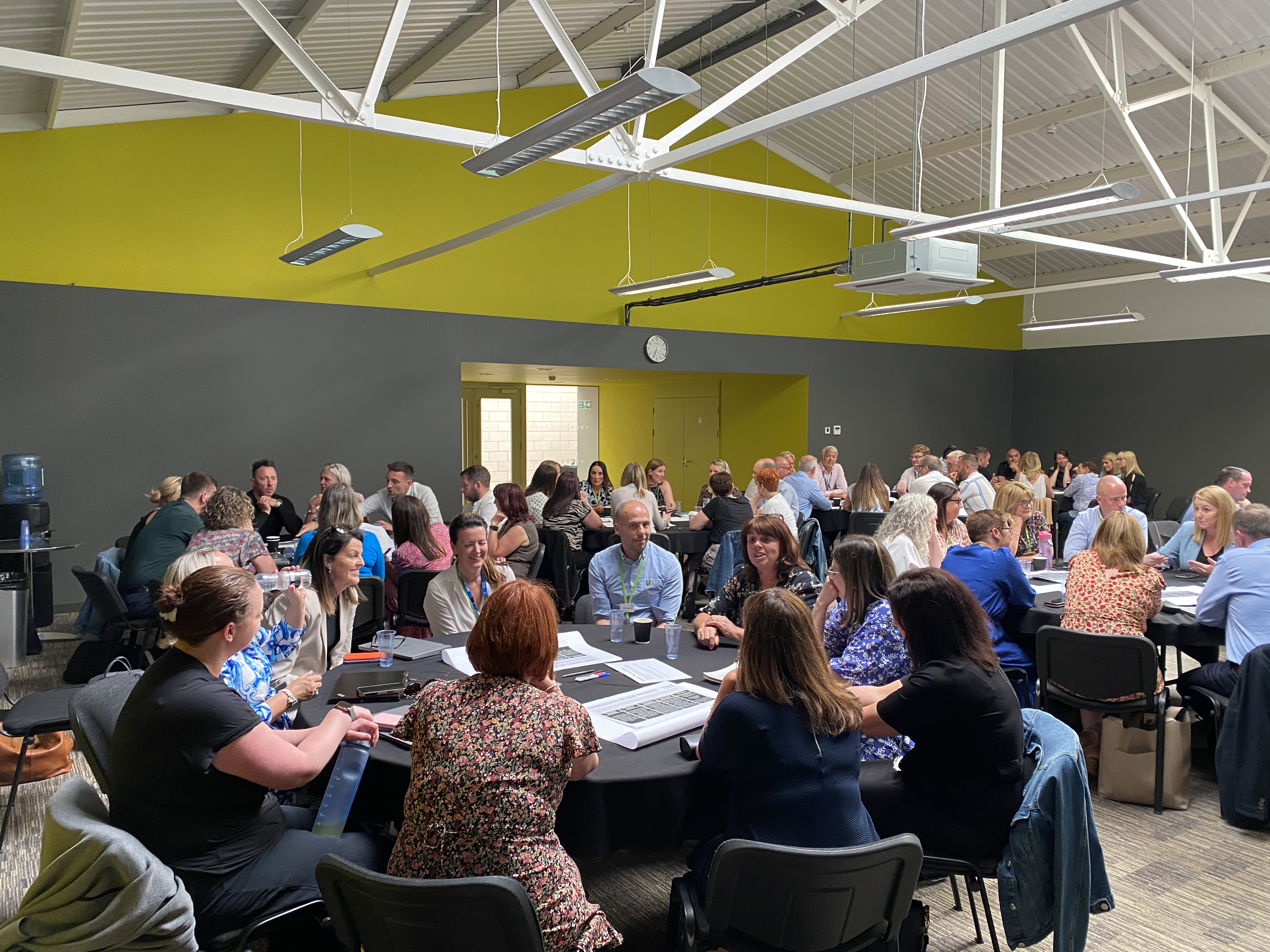 A picture of a room full of people having conversations around a few tables